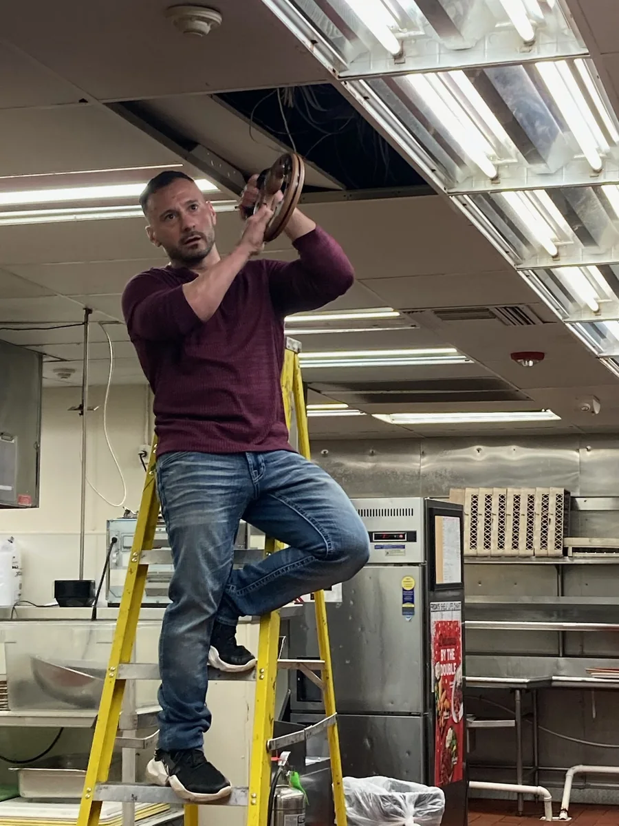 Michael P. Goodman on a ladder servicing ceiling infrastructure in a commercial kitchen