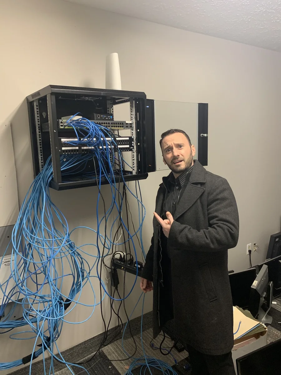 Michael P. Goodman beside an open network rack, tracing a tangle of cabling during an on-site infrastructure visit