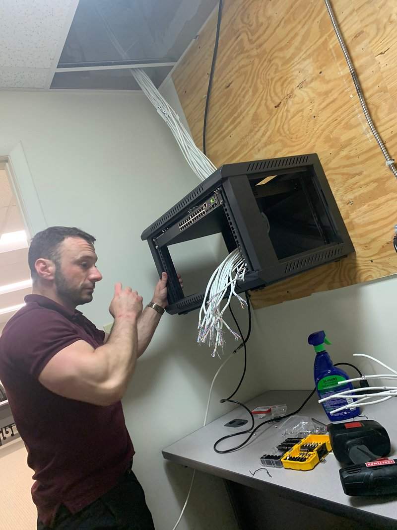 Michael P. Goodman mounting a network rack with a managed switch during an on-site IT install