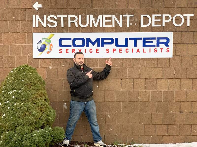 Michael P. Goodman pointing at the Computer Service Specialists sign on a brick building in snow