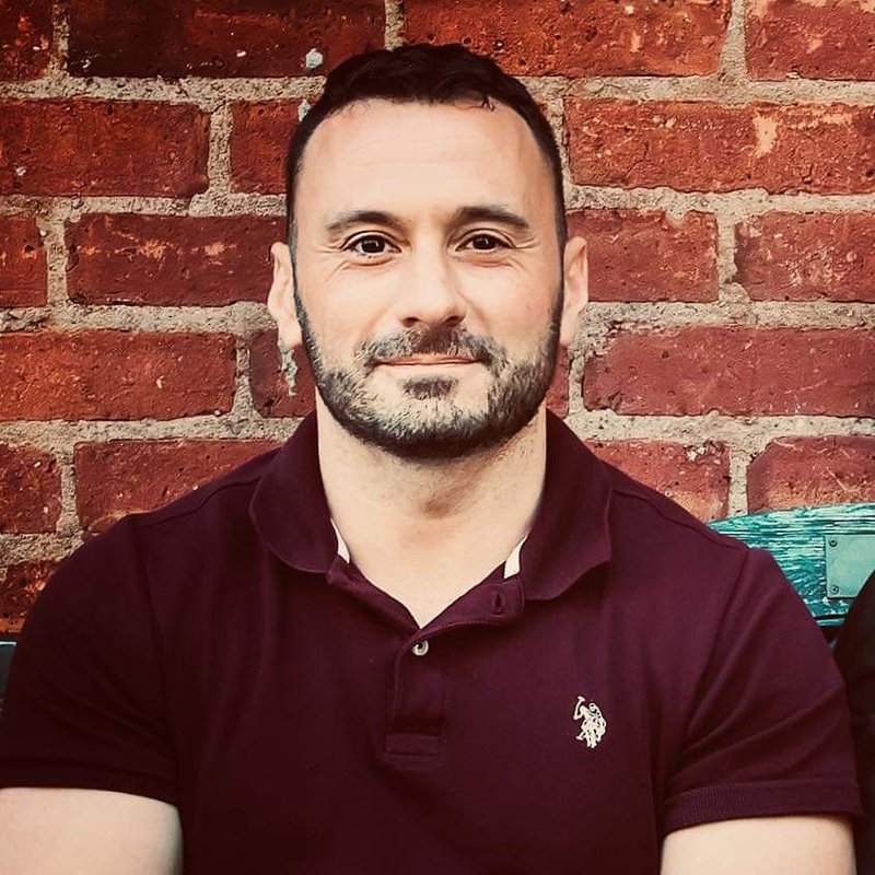 Portrait of Michael P. Goodman in a maroon polo shirt in front of a red brick wall
