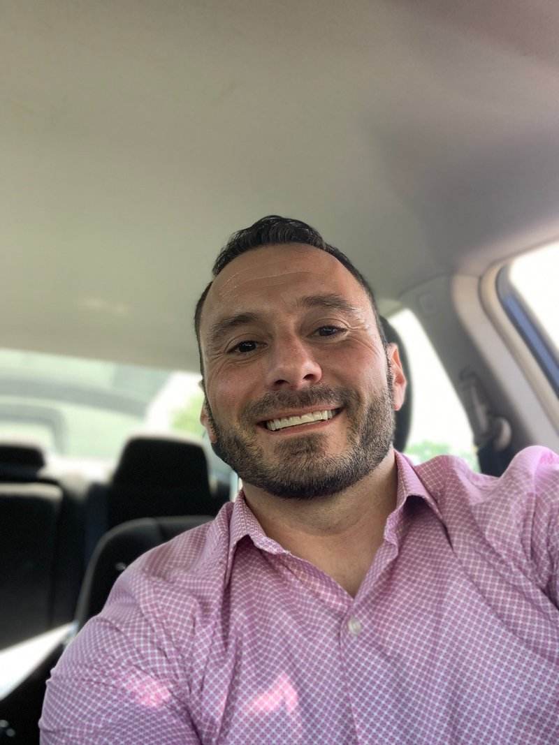 Michael P. Goodman smiling in a pink patterned button-up shirt, seated in a car